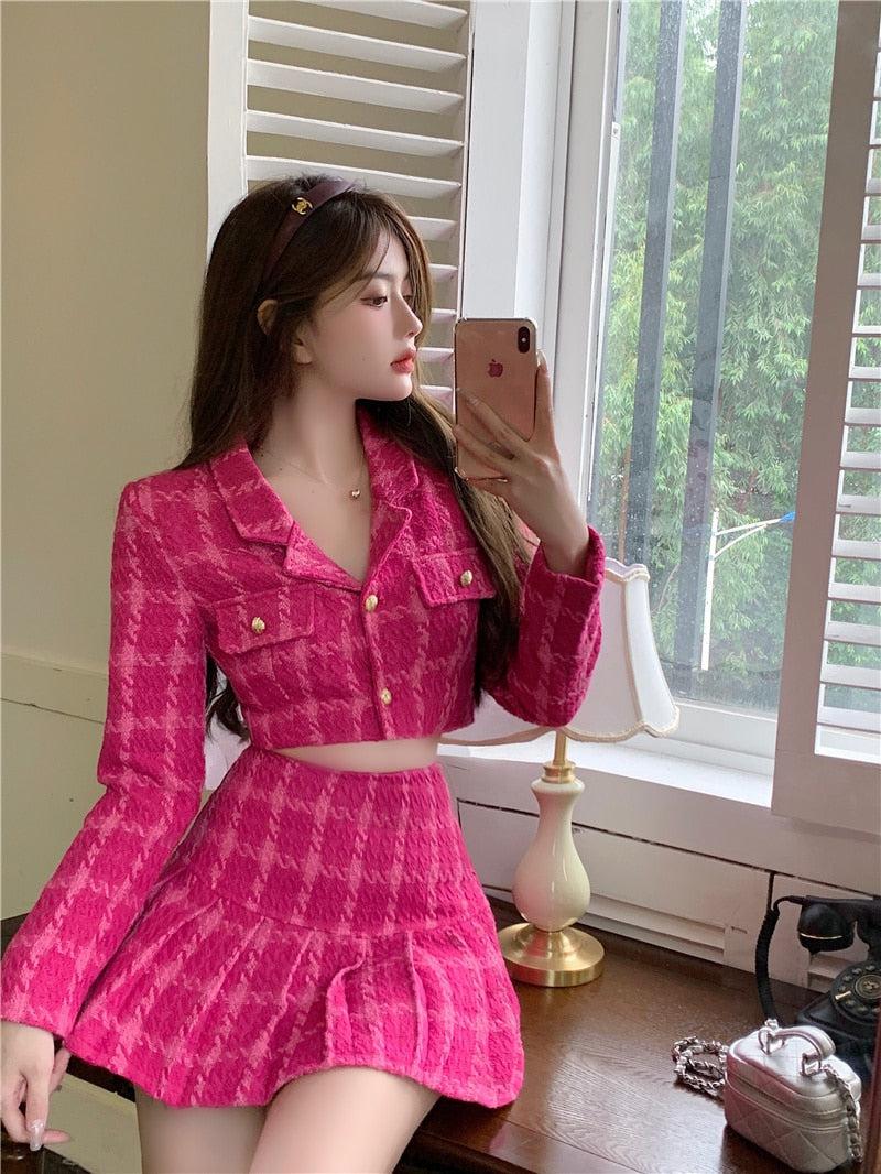 a girl wearing pink barbie crop jacket and mini skirt two piece set and she is holding her phone also she has a mini bag beside her