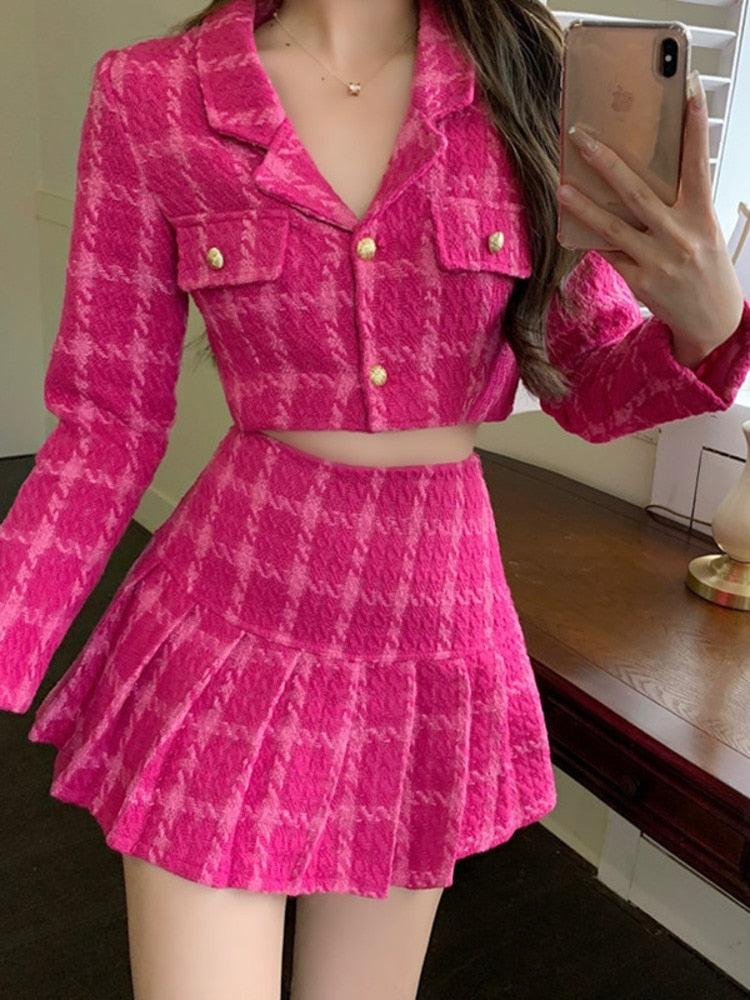 una chica con estética barbiecore lleva una chaqueta corta rosa de Barbie y un conjunto de dos piezas con minifalda y un collar dorado y sostiene su teléfono