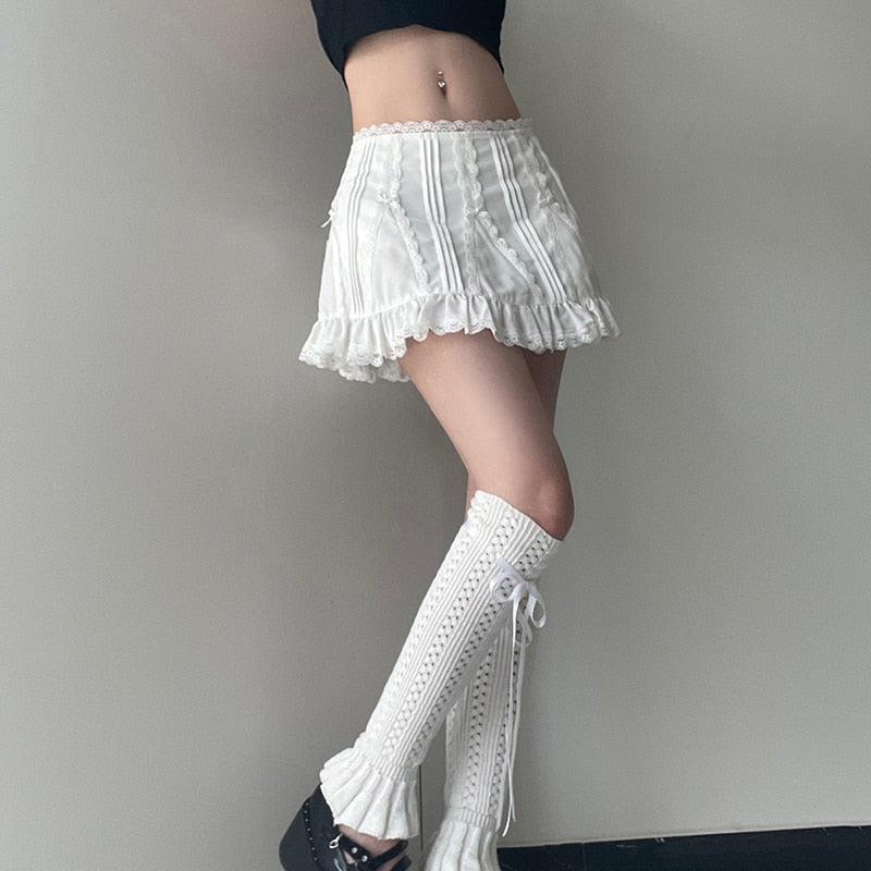 Una chica que lleva una minifalda blanca con volantes en el dobladillo y calcetines largos blancos con volantes y un top corto negro.
