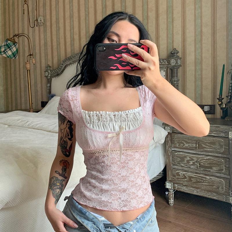 a girl who has tattoes on her arm wearing a pink and white coquette aesthetic lace detailed top and jeans