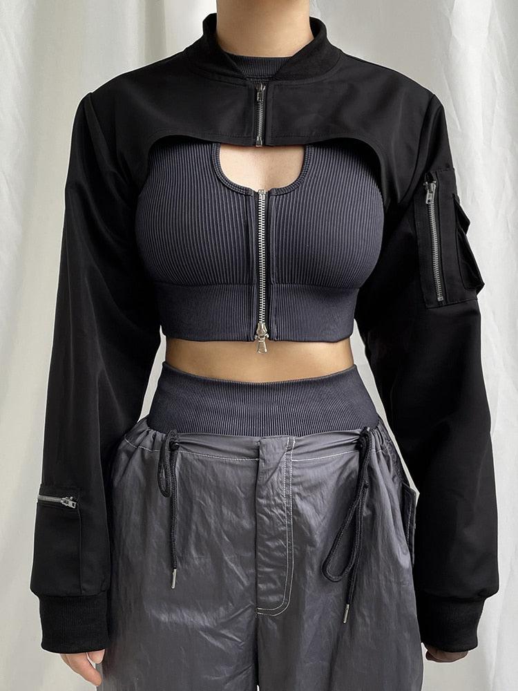 Una chica lleva una chaqueta bolero de estética cyberpunk en color negro y también lleva un top corto y pantalones grises.