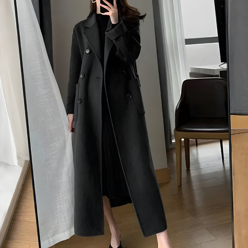 a girl is wearing a black dark academia belted long coat and a midi black dress