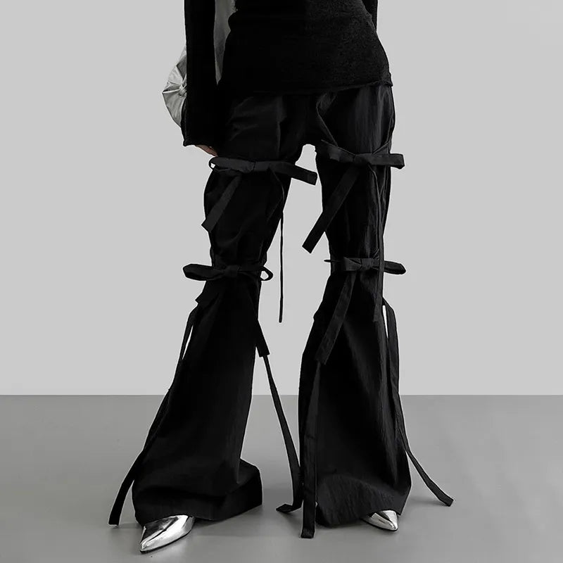 Una chica lleva unos alegres pantalones góticos acampanados con cordones en negro, una blusa negra y zapatos plateados.