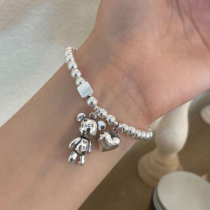 a girl is wearing a silver heart and bear bracelets, there are some words on the bear such as peace and love