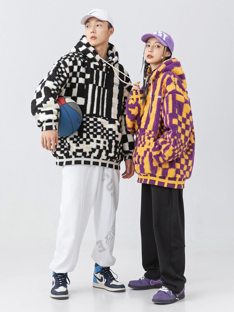 ein Mann und eine Frau, die übergroße Plüsch-Kapuzenpullis tragen; Der Kapuzenpullover für Männer ist schwarz und weiß, während der Kapuzenpullover für Frauen lila und orange ist