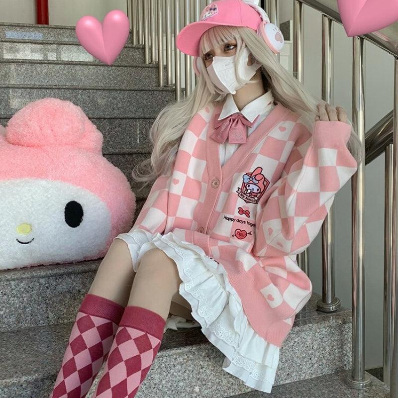 Una chica con estética kawaii lleva un cárdigan rosa y blanco abotonado de My Melody y un sombrero rosa y una falda blanca y calcetines a cuadros rosas y rojos y auriculares rosas y también hay un peluche de My Melody en las escaleras en el que está sentada.
