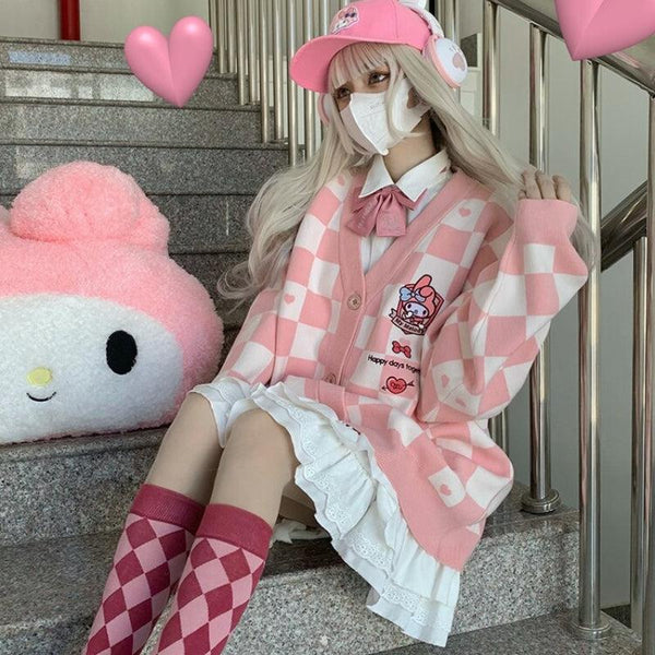 une fille à l'esthétique kawaii porte un cardigan rose et blanc my melody à boutons, un chapeau rose, une jupe blanche, des chaussettes à carreaux roses et rouges, un casque rose, et il y a aussi une peluche my melody sur les escaliers où elle est assise