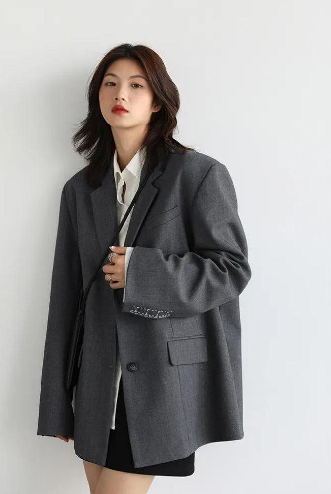 Office style wide-shoulder classy gray blazer for women, styled with a white shirt and black skirt, showcasing a chic and professional aesthetic.