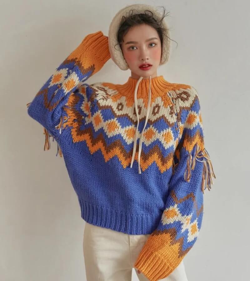 a twee aesthetic girl is wearing a retro pattern knitted christmas sweater in blue, orange, brown and cream, and white pants