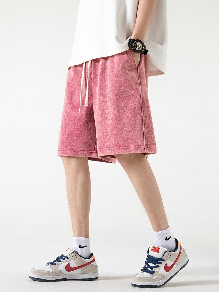 Un niño con pantalones cortos deportivos rosas suaves con cordón en la cintura, una camisa blanca, calcetines y zapatillas Nike.