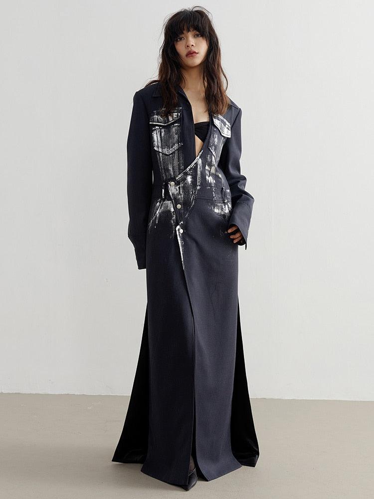 Model wearing a black and white distressed long blazer with maxi length, featuring chest and hip pockets, button fastening, and bold grunge-inspired design details.