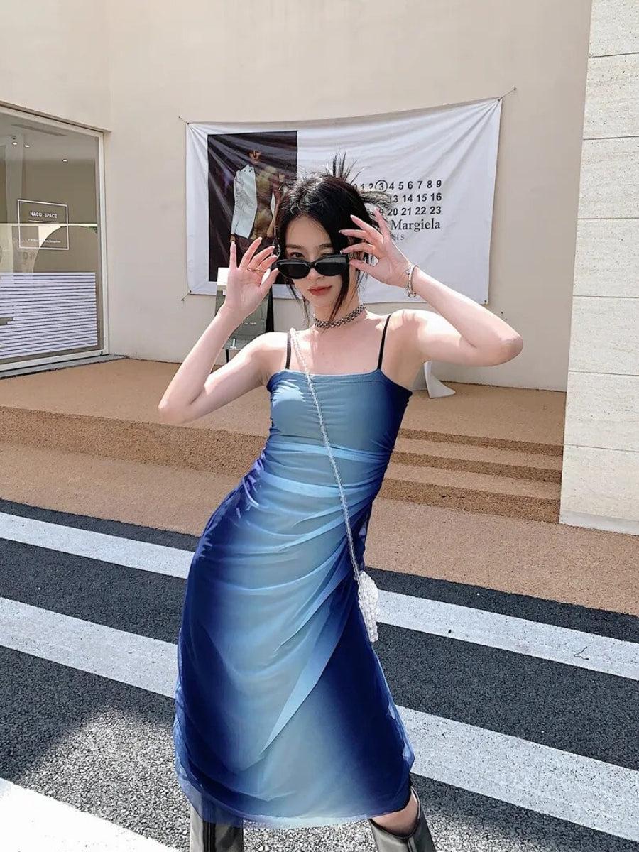 a girl is wearing a y2k blue gradient strappy midi dress and a white mini bag and sunglasses